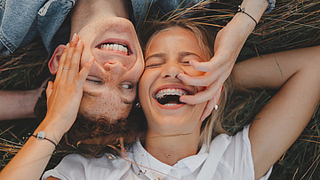 Zwei Teeanger liegen auf einer Wiese, sie hat eine feste Zahnspange.