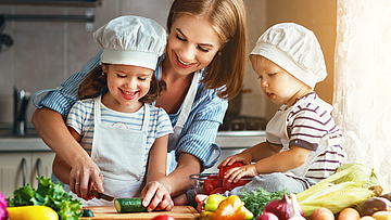 Die Haushaltshilfe der Familie bereitet mit den Kindern das Essen vor.