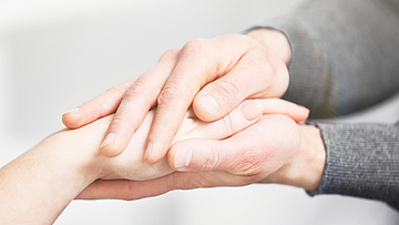 Die Hände einer jungen Person umfassen eine Hand einer älteren Person.