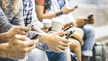 Eine Gruppe junger Menschen sitzt auf einer Mauer. Sie alle haben Smartphones in der Hand und schauen darauf. 