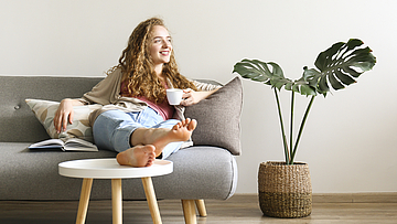 Junge Frau sitzt zufrieden auf dem Sofa denn sie war bei der Krebsvorsorge.