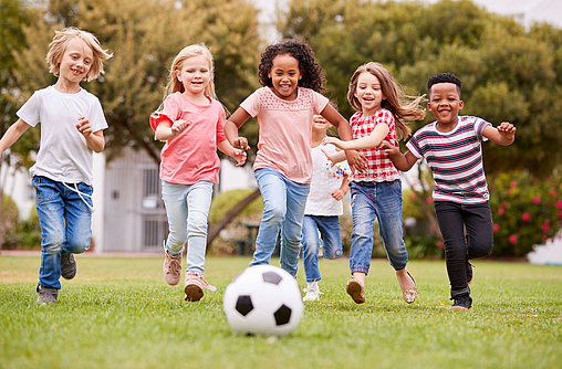 Zur Stärkung des Immunsystems bei Kindern rennen ein paar Mädchen und Jungen einem Fußball hinterher