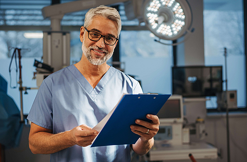 Porträt eines selbstbewussten Arztes, der in der Notaufnahme im Krankenhaus steht. Ein ansprechender Arzt, der sich in einer modernen Privatklinik befindet, in Pediküren, die Zwischenablage halten.