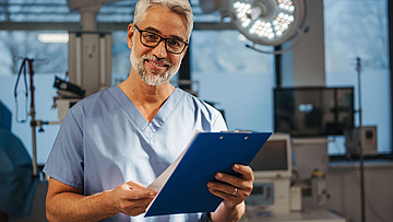 Porträt eines selbstbewussten Arztes, der in der Notaufnahme im Krankenhaus steht. Ein ansprechender Arzt, der sich in einer modernen Privatklinik befindet, in Pediküren, die Zwischenablage halten.