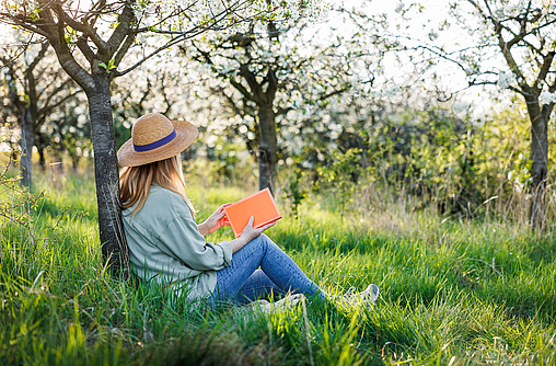 Junge Frau sitzt auf einer Wiese und liest ein Buch bei ihrer Digital Detox Erfahrung