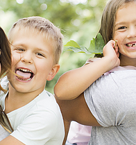 Junge Familie im Park. Die Mutter trägt den Sohn und der Vater trägt die Tochter huckeback.