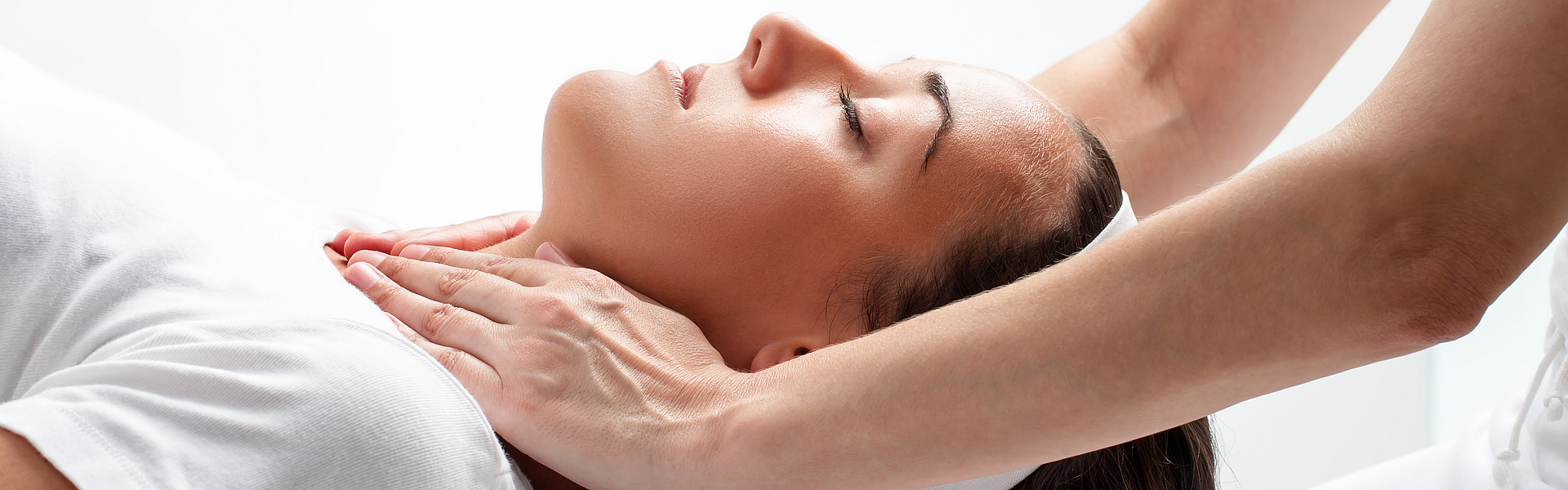 Eine Frau wird von einem Osteopathen behandelt. Er löst mit seinen Händen eine Blockade im Hals-Schulter-Bereich.