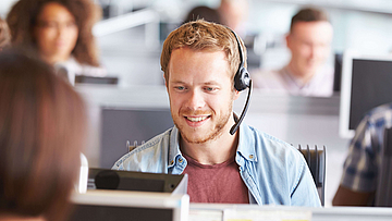 In einem Callcenter sitzt ein junger Mann und berät online eine Kundin.