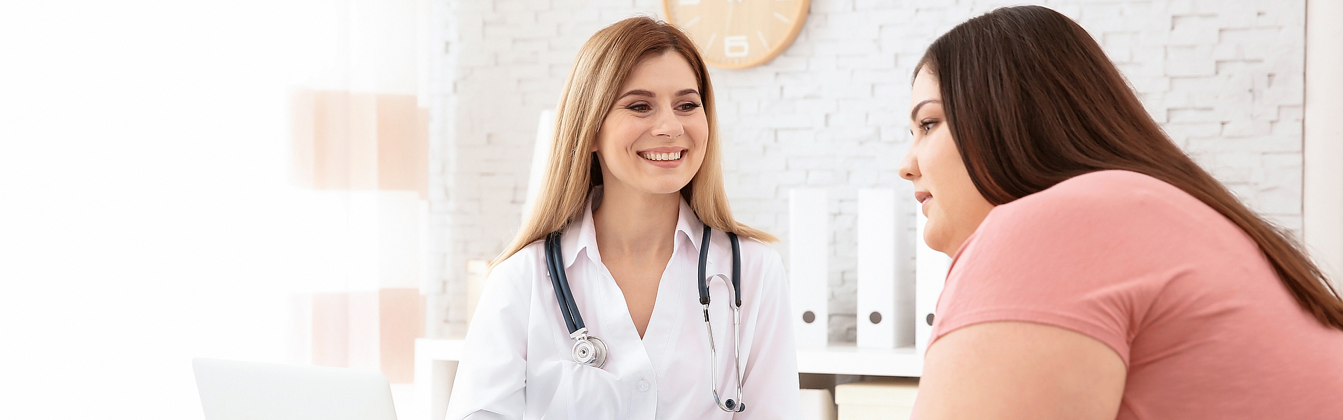 Eine dicke junge Frau sitzt ihrer Ärztin gegenüber und besprechen etwas.
