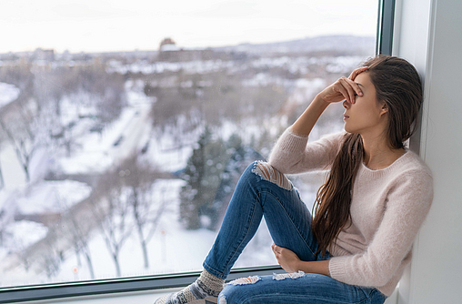 Frau vor einem Fenster ist antriebslos wegen des Winterblues.