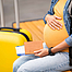 Schwangere Frau mit Koffer und Flugticket
