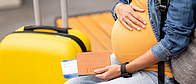 Schwangere Frau mit Koffer und Flugticket