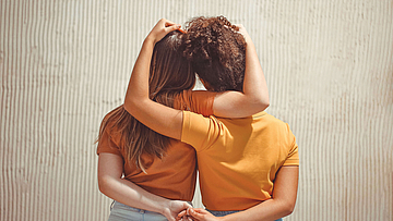 Rückansicht von zwei Mädchen die sich an den Händen halten und umarmen.