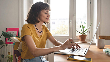 Frau ist im Homeoffice, sie sitzt mit geöffnetem Laptop am Esszimmertisch.