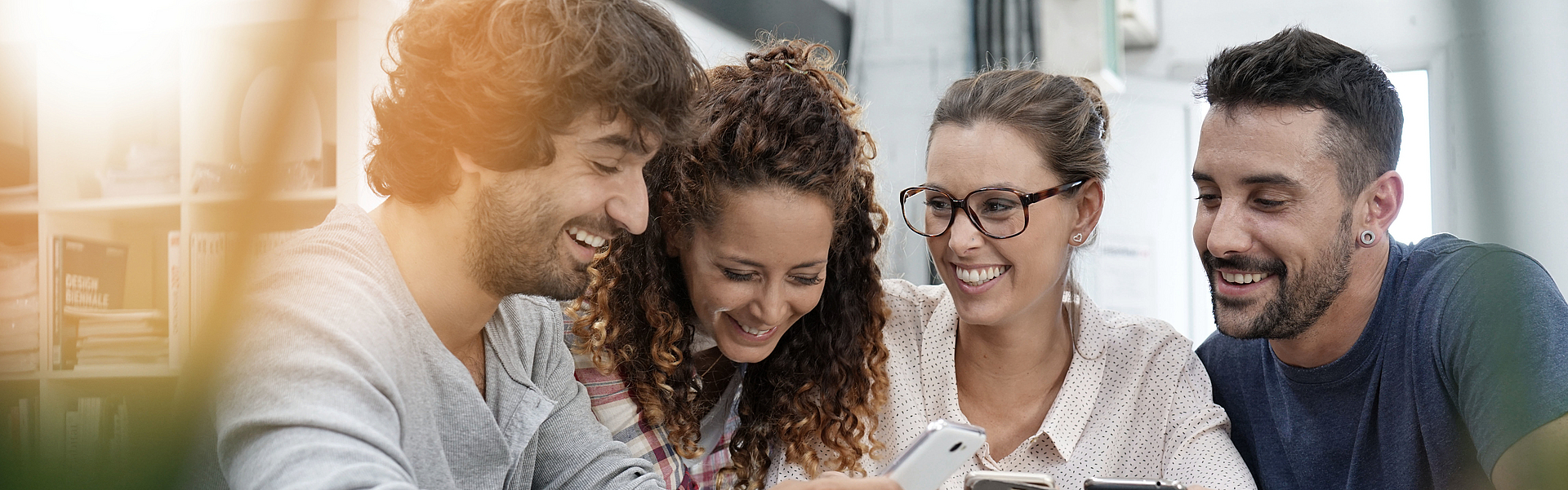 Zwei glückliche Paare sitzen am Tisch und schauen gemeinsam in ihre Handys.