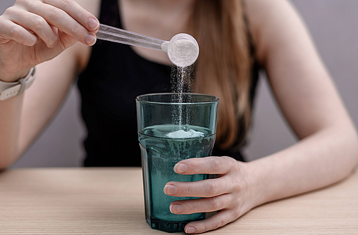 Frau löst Kreatin in einem Glas Wasser auf.