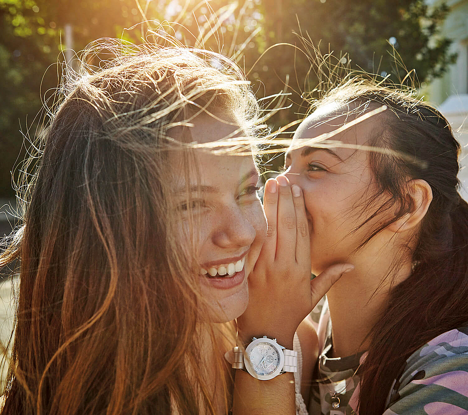 Mädchen flüstert einem anderem Mädchen etwas ins Ohr