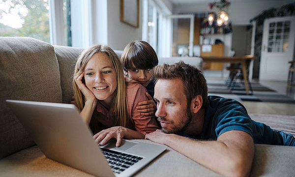 Fröhliche Familie auf dem Sofa mit Laptop.