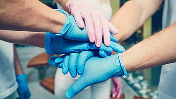 Pflegende Hände mit Handschuhen symbolisieren Zusammenarbeit der Pflegekräfte.