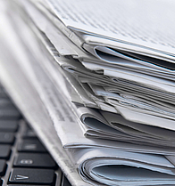Headerfoto_Presse-Übersichtsseite_Zeitungen_Laptop Stapel Zeitungen liegt auf der Tastatur eines geöffneten Laptops