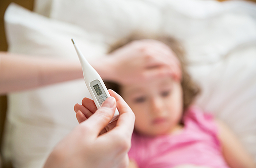 Ein kranken Kind liegt im Bett. Es hat hohes Fieber. Die Mutter hält ein digitales Fiebertermometer. Das ist im Closeup zu sehen.