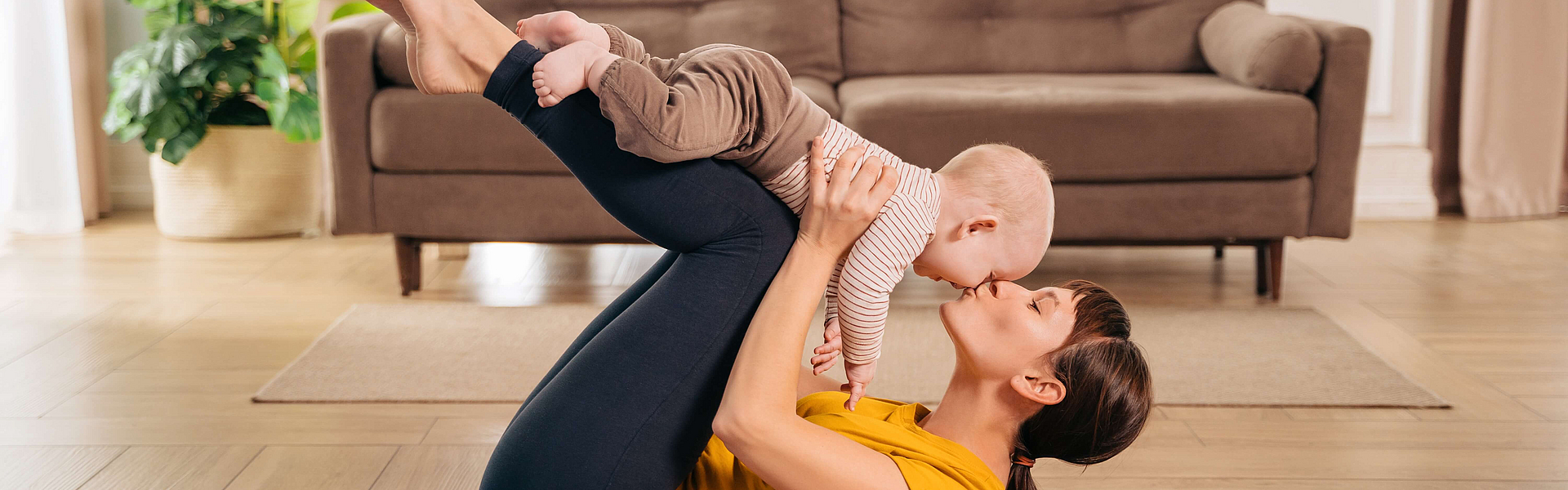 Eine Frau hält ein Baby hoch und führt dabei eine Übung zur Rückbildung des Beckenbodens aus