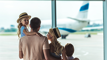 Eine Familie ist im Flughafen und schaut aus dem Fenster auf ein Flugzeug.