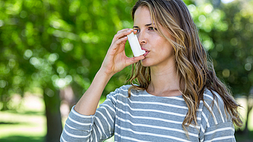 Eine Frau ist im Garten und benutzt ein Asthmaspray.