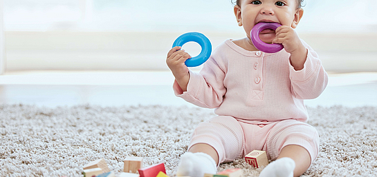 Baby steckt sich einen Beißring in den Mund, um die Schmerzen beim Zahnen und somit mögliche Hautausschläge zu reduzieren