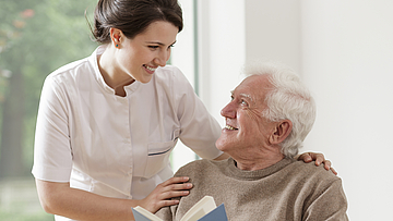 Ältere Mann mit einem Buch wird von einer Frau gepflegt.
