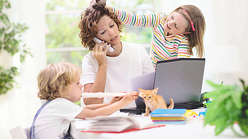 Eine Mutter arbeitet im Homeoffice. Die Tochter spielt mit einem Dinosaurier auf ihrem Kopf. Der Junge spielt Blockflöte. Die Mutter ist genervt, denn sie telefoniert.