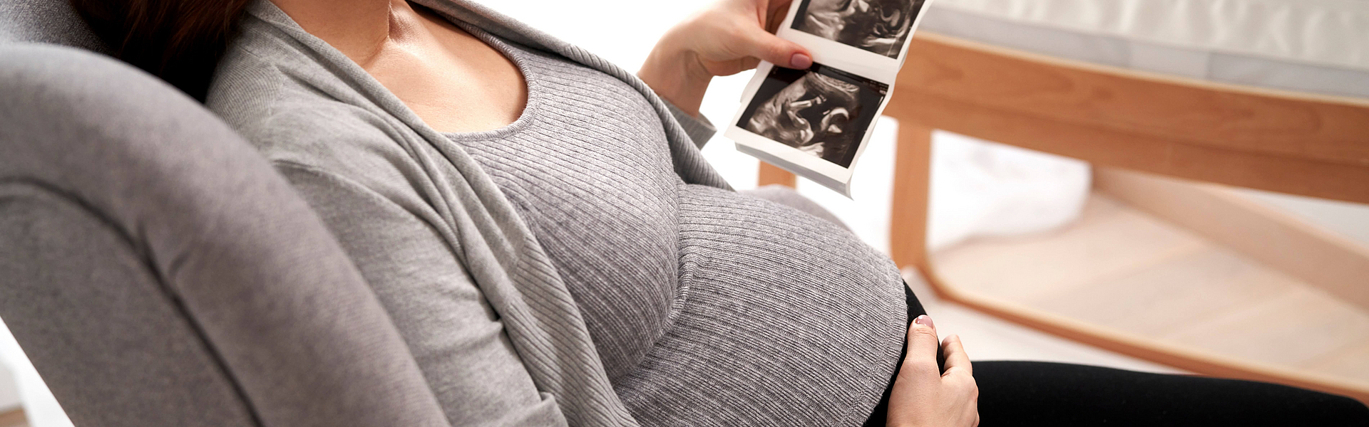 Schwangere Frau sitzt im Sessel und betrachtet ihr Ultraschall