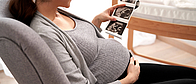 Schwangere Frau sitzt im Sessel und betrachtet ihr Ultraschall