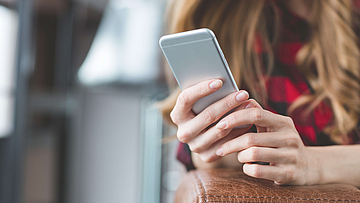 Blonde Frau mit einem Smartphone in der Hand. Man kann nur die Hände und das Smartphone sehen.