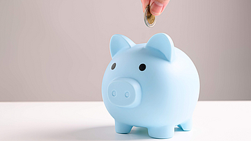 Hand steckt Kleingeld in blaues Sparschwein