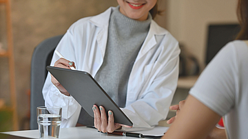 Ein Arztgespräch mit Patient. Der Arzt hat ein Tablet in der Hand und zeigt etwas dem Patienten.