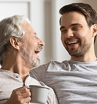 Ein Rentner und ein Mann sitzen lachend auf dem Sofa.