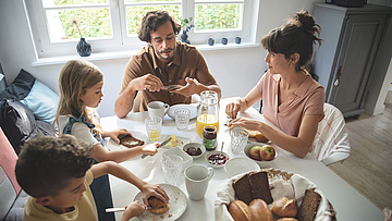 Eine Familie sitzt gemeinsam am Frühstückstisch und genießen das gemeinsame Essen.