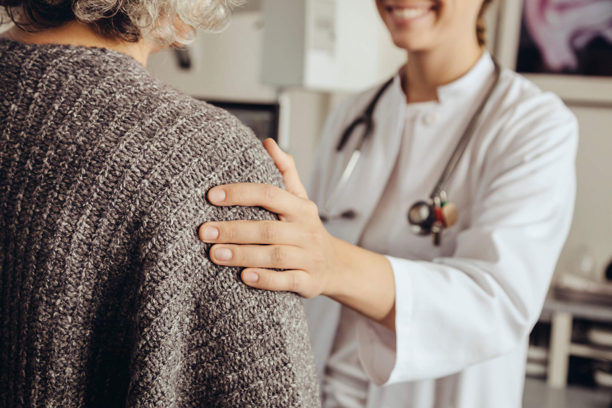 Lächelnde Ärztin berührt Patientin beruhigend mit der Hand.