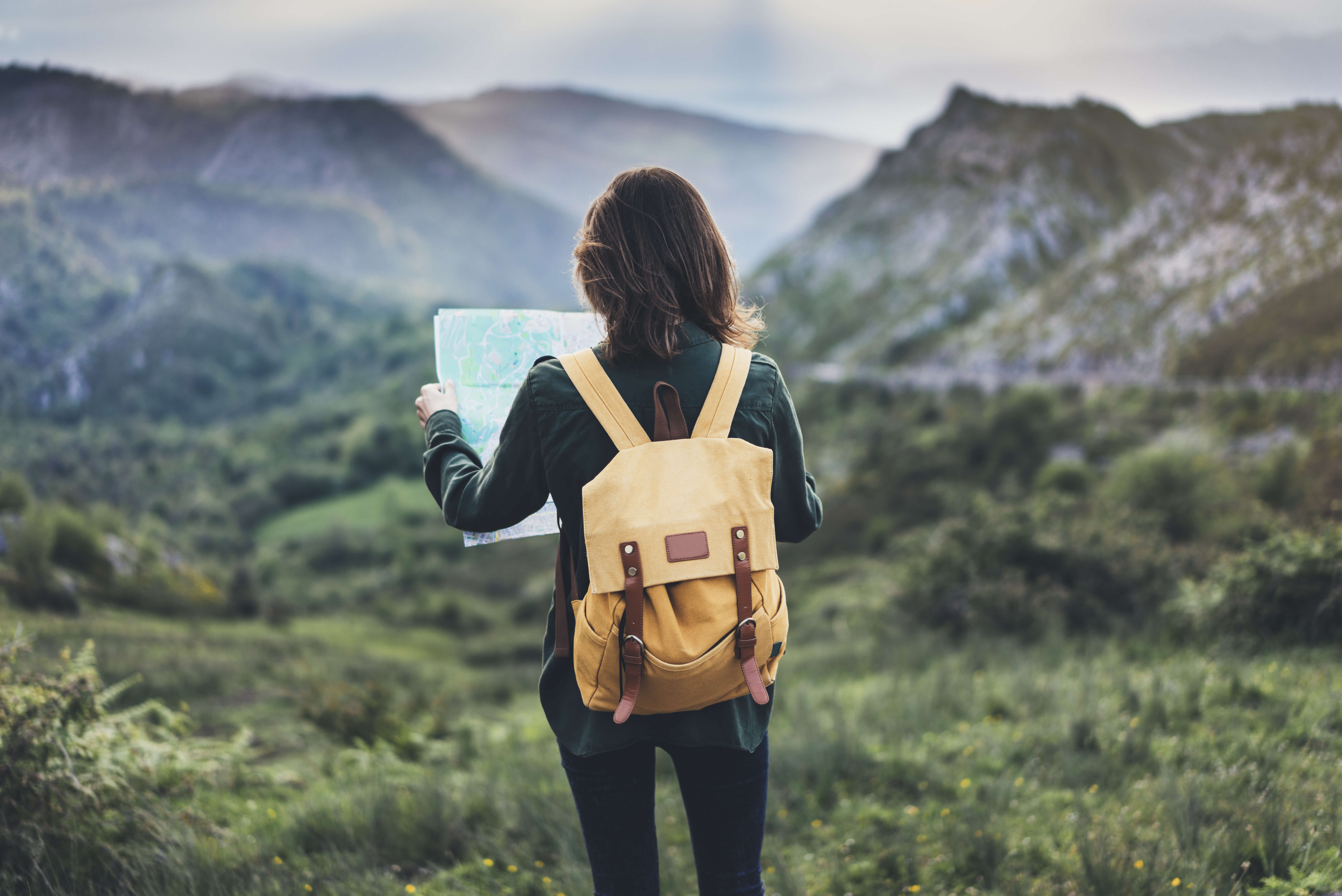 Mädchen mit Rucksack auf einem Berggipfel und schaut auf eine Karte